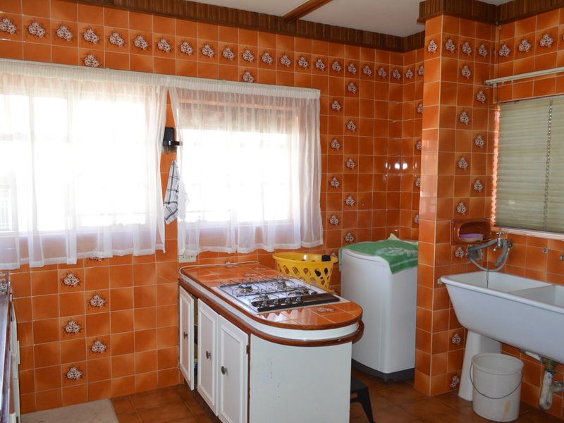 A dated kitchen featuring orange decorative wall tiles, built-in cabinetry, a gas hob, and a traditional ceramic sink.