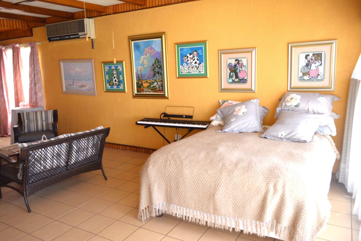 Spacious bedroom featuring tiled flooring, timber ceiling beams, and a wall-mounted air conditioning unit.
