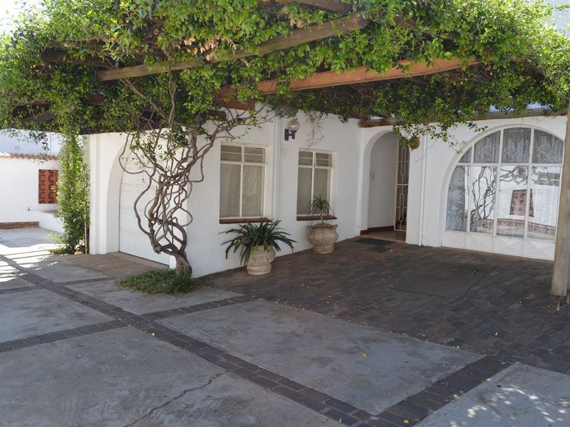 Front exterior view of the townhouse featuring a paved driveway, arched window, and a large timber pergola covered in climbing vines.