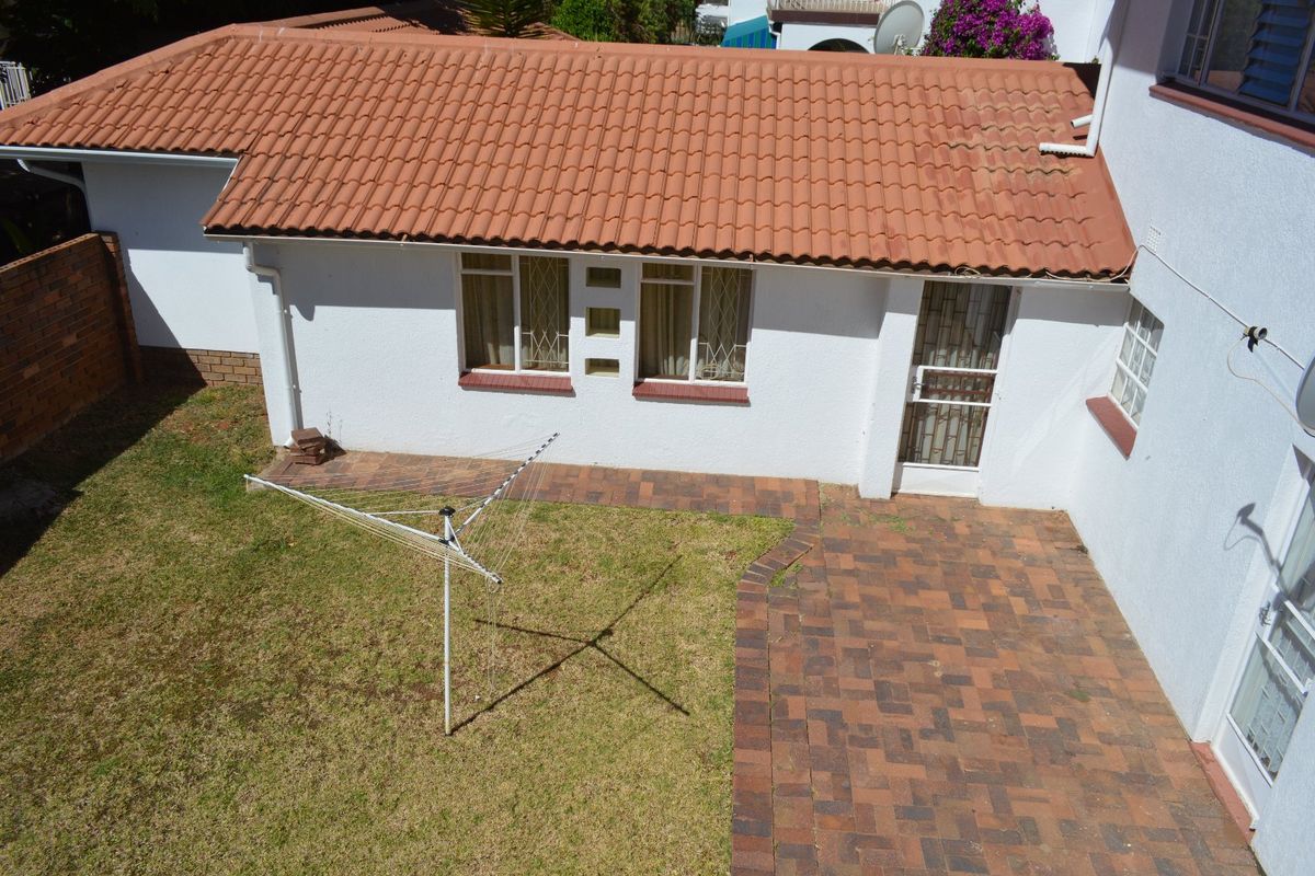 Rear view of the townhouse featuring a terracotta tiled roof, brick paved patio area, and a small private garden with security features.