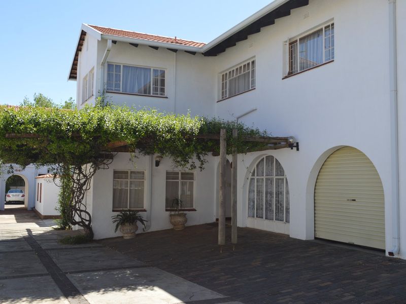 Front elevation of a townhouse featuring a paved driveway, arched garage entrance, and a characterful timber pergola with climbing greenery.