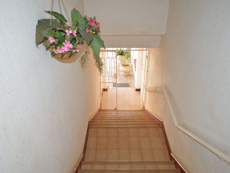 A tiled staircase leading to a secure entrance gate, featuring a metal handrail and neutral wall finishes.