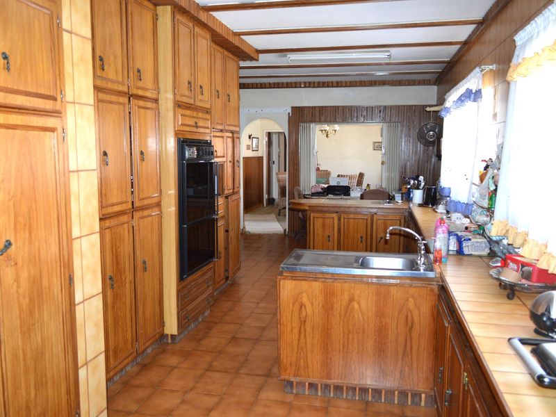 A dated kitchen featuring extensive wooden cabinetry, a double wall oven, tiled countertops, and exposed ceiling beams, offering significant potential for a modern renovation.