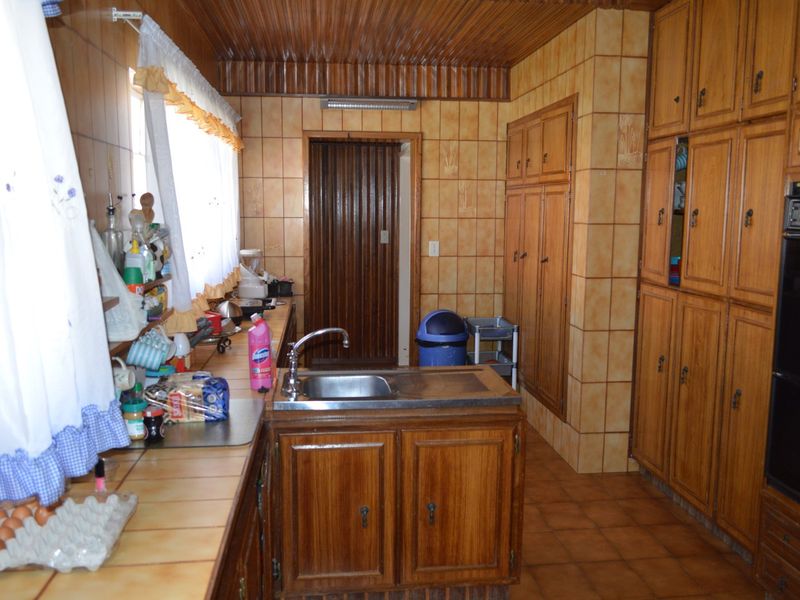 A dated kitchen featuring extensive built-in wooden cabinetry, tiled countertops, and a built-in oven, offering a traditional layout with significant renovation potential.