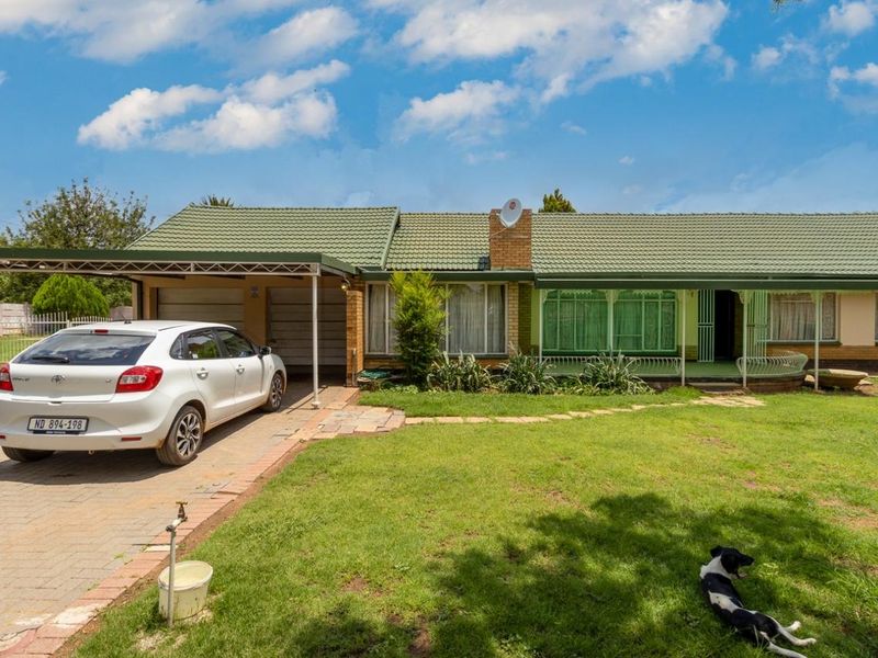 Front elevation of a single-story house featuring a tiled roof, attached carport, paved driveway, and a well-maintained front lawn.
