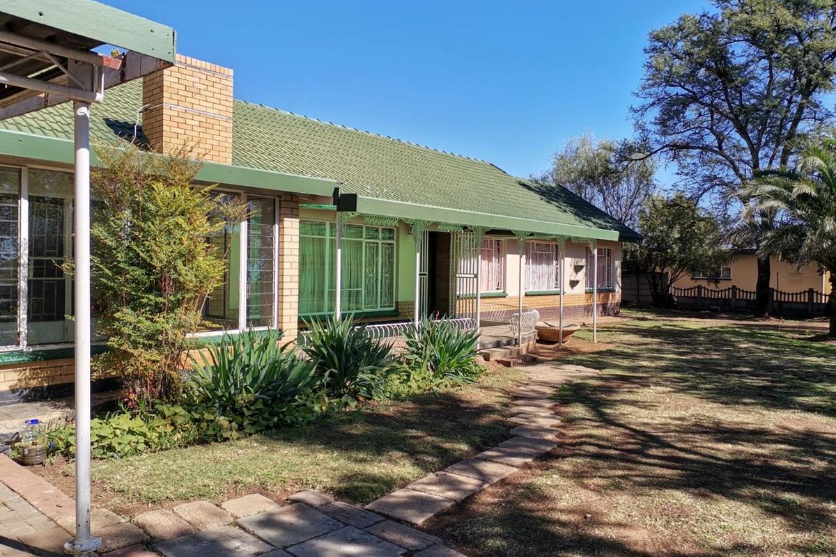 Rear view of a brick house featuring a covered patio, tiled roof, and a stone pathway leading through the garden.