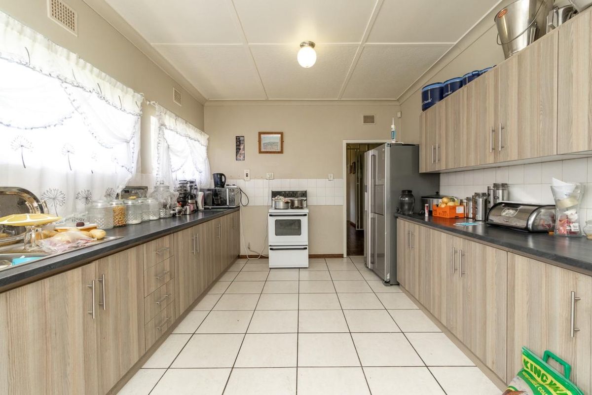 A functional galley-style kitchen featuring light wood-look cabinetry, dark laminate countertops, tiled flooring, and a freestanding stove with a tiled backsplash.