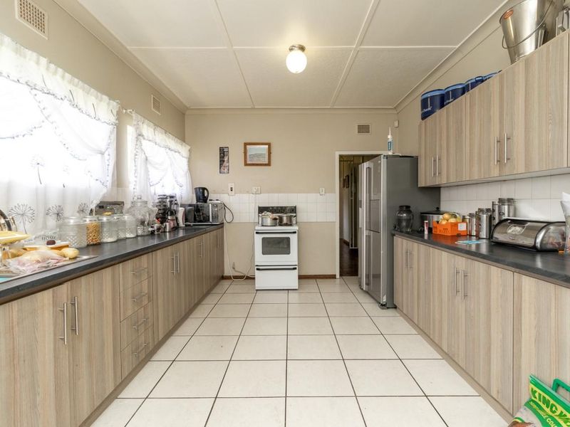 A functional galley-style kitchen featuring light wood-look cabinetry, dark laminate countertops, tiled flooring, and a freestanding stove with a tiled backsplash.