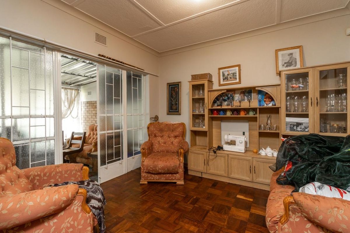 A living room featuring classic parquet flooring and sliding glass doors that provide access to an adjacent covered patio area.