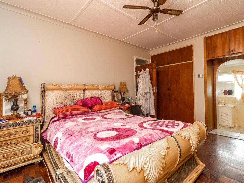 A bedroom featuring built-in wooden cupboards, a ceiling fan, and an arched entryway leading to an en-suite bathroom.
