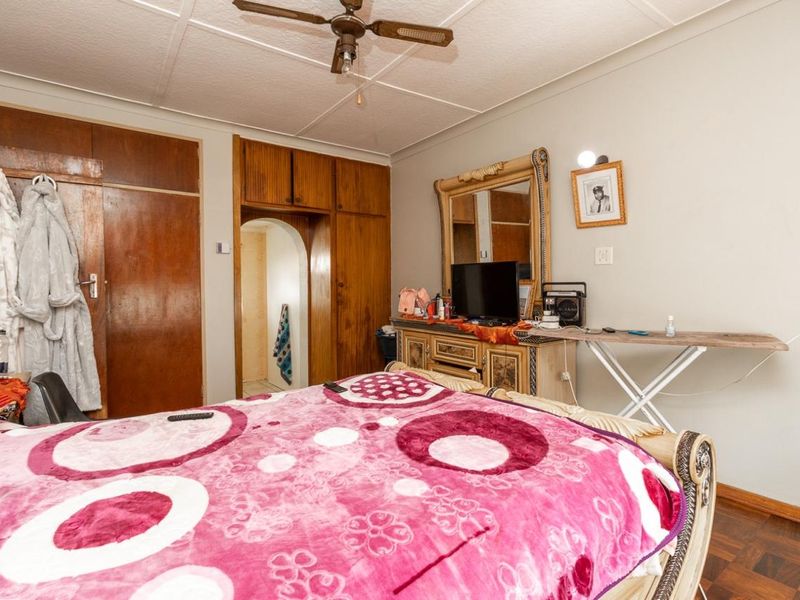 A bedroom featuring parquet flooring, built-in wooden cupboards, and a ceiling fan, with an arched doorway leading to an adjacent space.
