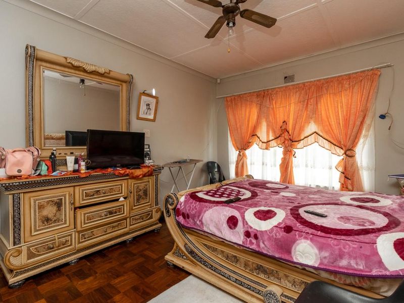 A bedroom featuring classic parquet flooring, a ceiling fan, and neutral wall finishes, offering a functional space with potential for modern updates.