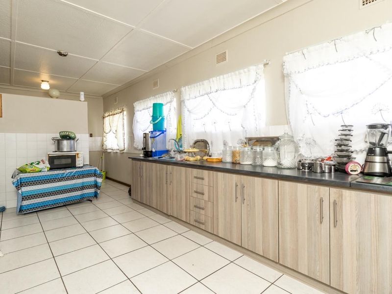 A functional kitchen featuring light wood-look cabinetry, dark laminate countertops, tiled flooring, and a tiled splashback with ample natural light.