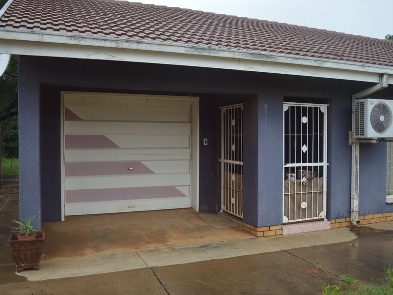 Front exterior view featuring a single garage, security gates, and a wall-mounted air conditioning unit under a tiled roof.