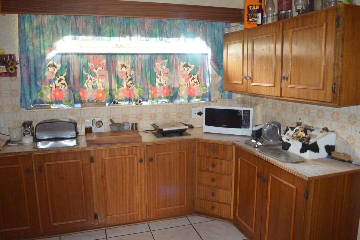 A dated kitchen featuring traditional wooden cabinetry, tiled backsplash, and tiled flooring, offering a functional layout with ample storage space.
