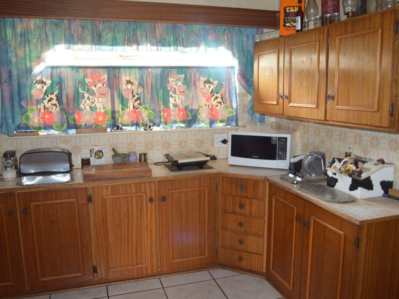 A dated kitchen featuring traditional wooden cabinetry, tiled backsplash, and tiled flooring, offering a functional layout with ample storage space.