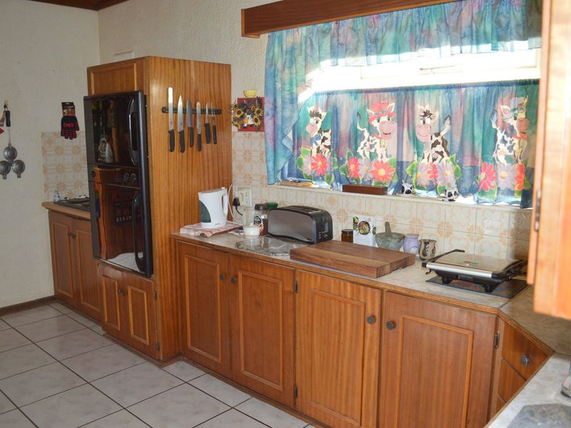 A dated kitchen featuring traditional wooden cabinetry, tiled backsplash, and tiled flooring, offering a functional layout with potential for modern renovation.