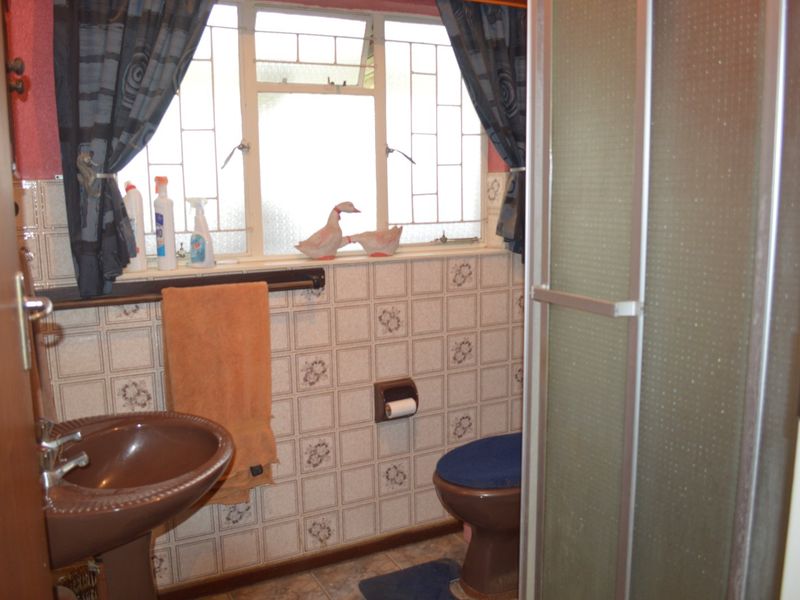 A dated bathroom featuring a brown pedestal basin, toilet, and shower enclosure with patterned wall tiles and a window.