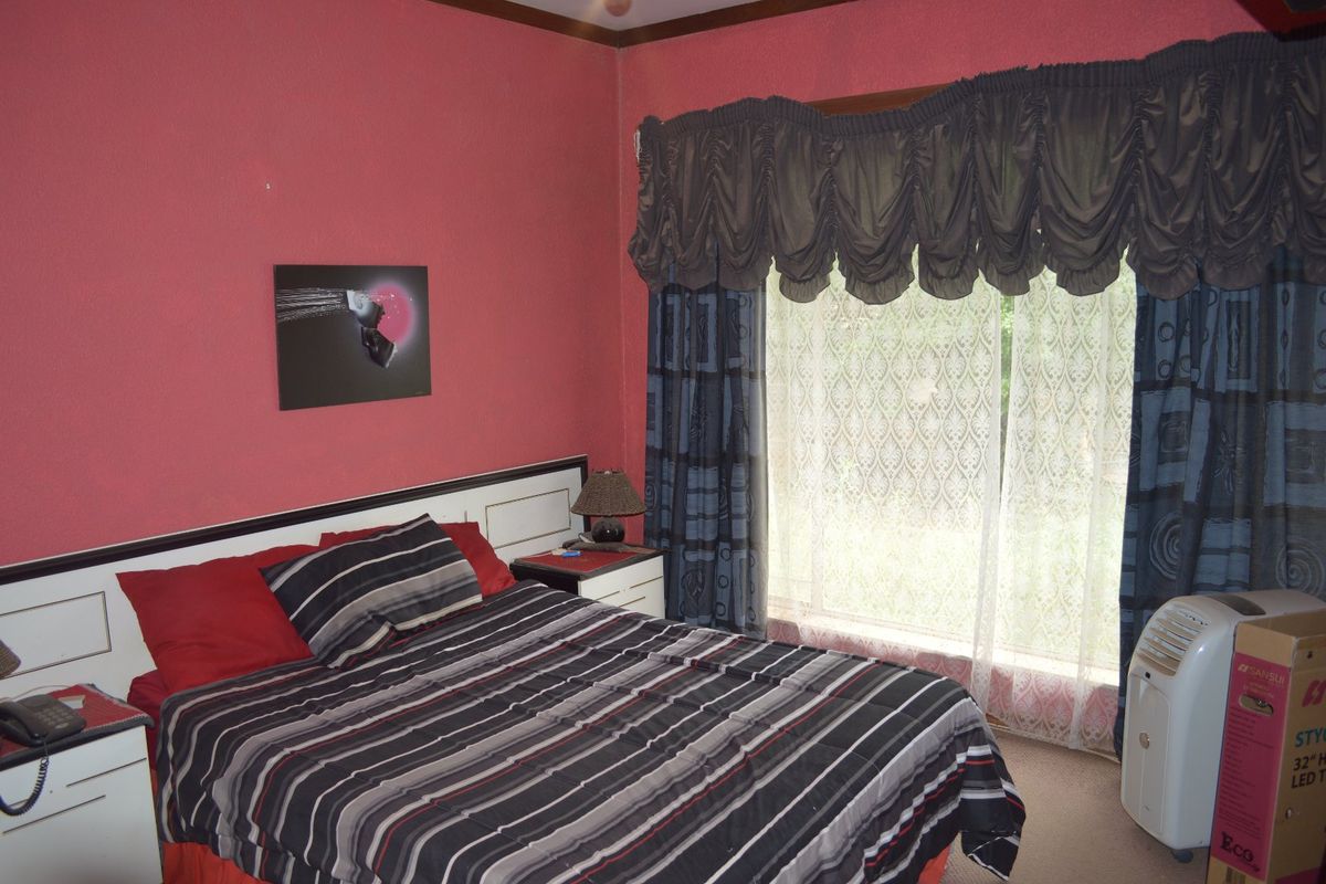 A bedroom featuring a built-in headboard, carpeted flooring, and a large window with decorative curtains.