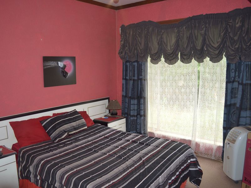 A bedroom featuring a built-in headboard, carpeted flooring, and a large window with decorative curtains.