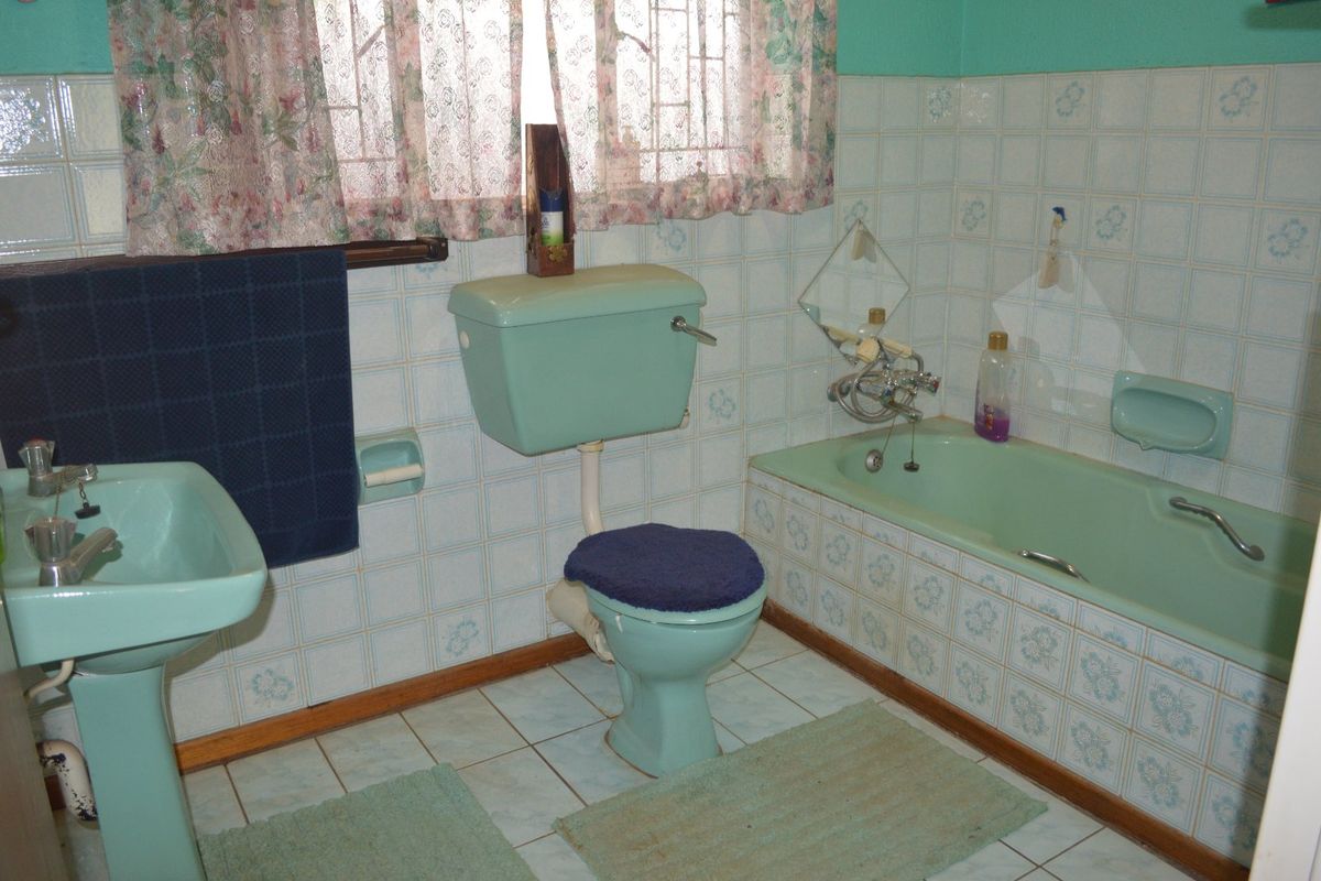 A dated bathroom featuring original pastel green sanitaryware, including a pedestal basin, low-level toilet, and built-in bathtub with matching ceramic wall tiling.