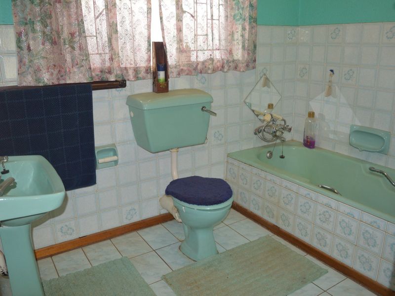A dated bathroom featuring original pastel green sanitaryware, including a pedestal basin, low-level toilet, and built-in bathtub with matching ceramic wall tiling.