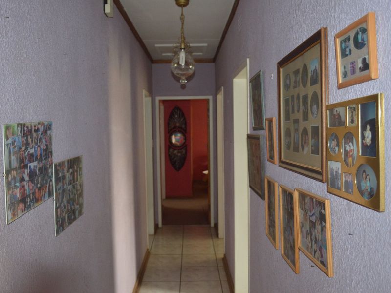 A narrow residential hallway featuring tiled flooring and a central pendant light fixture, providing access to multiple rooms.