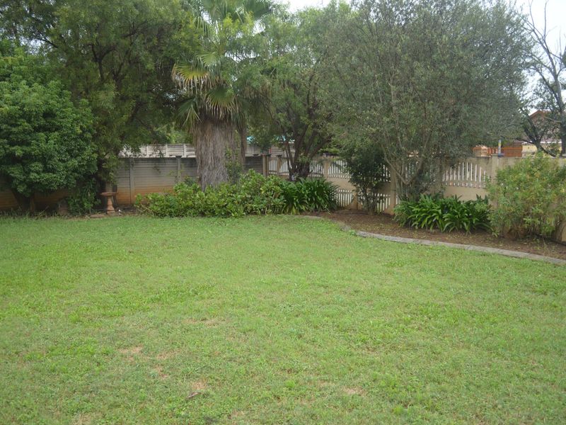 A spacious private garden featuring a lawn, mature trees, and established perimeter fencing with concrete and picket elements.