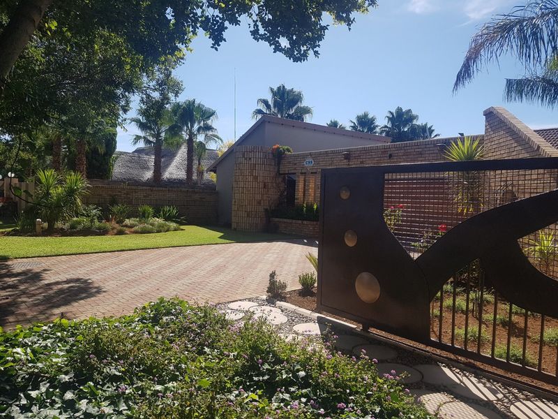 Front view of the property featuring a paved driveway, landscaped garden, and a modern metal security gate leading to the brick-faced residence.