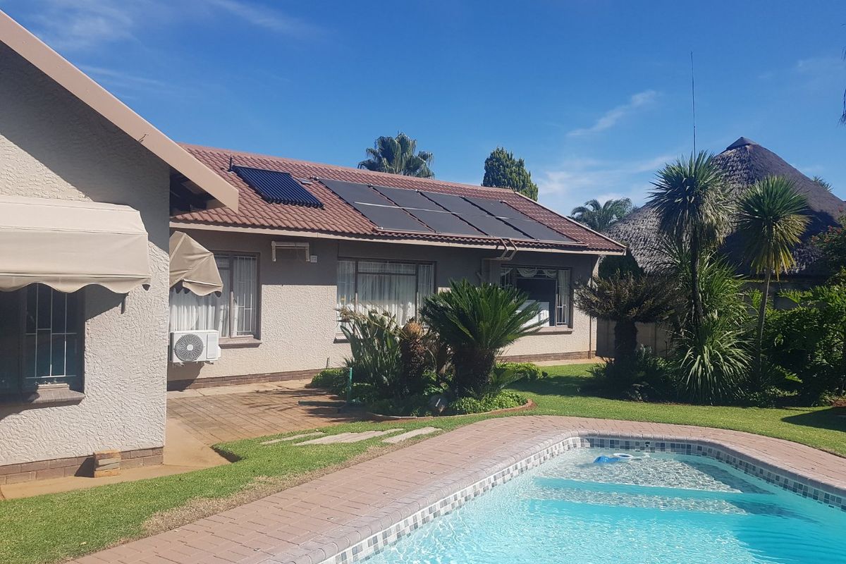 Rear exterior view featuring a swimming pool, paved patio area, and solar water heating panels installed on the tiled roof.