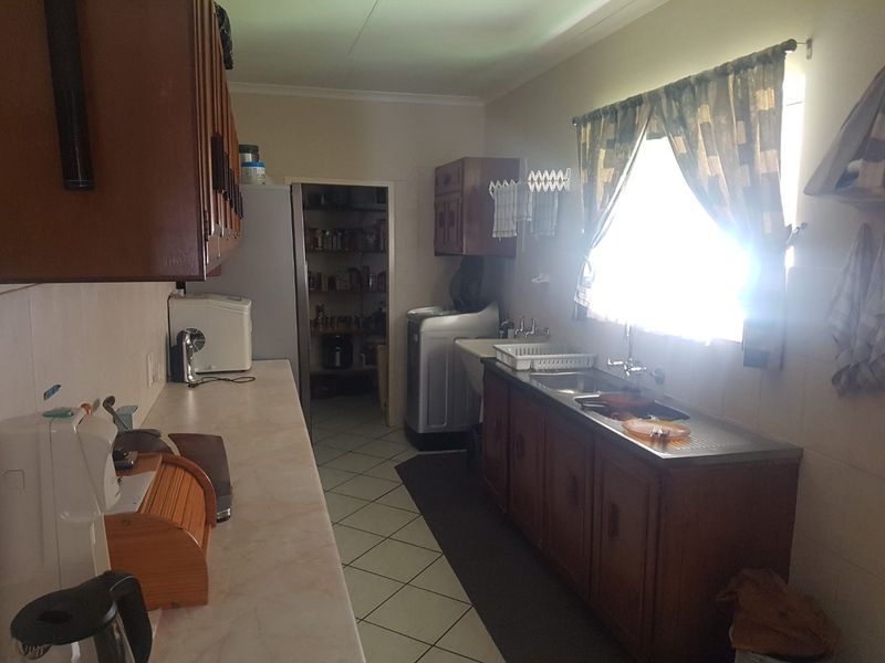 A functional scullery area featuring built-in wooden cabinetry, a stainless steel sink, and a dedicated pantry space with tiled flooring.