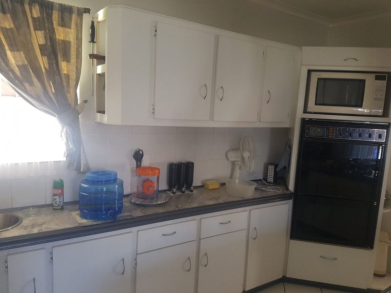 A functional kitchen featuring white built-in cabinetry, a tiled backsplash, and integrated oven and microwave units with laminate countertops.