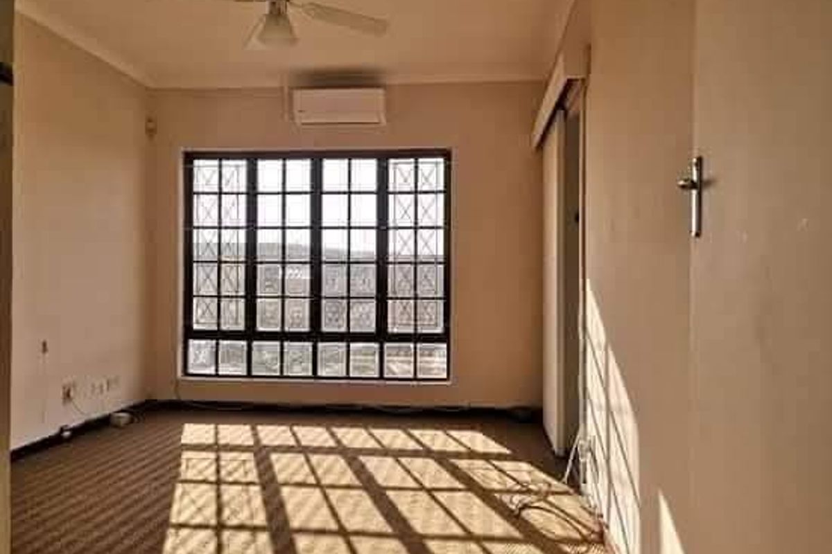 An empty living room featuring a ceiling fan, split-system air conditioning, and large windows with security bars, finished with carpet flooring.