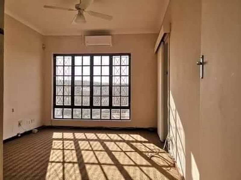 An empty living room featuring a ceiling fan, split-system air conditioning, and large windows with security bars, finished with carpet flooring.