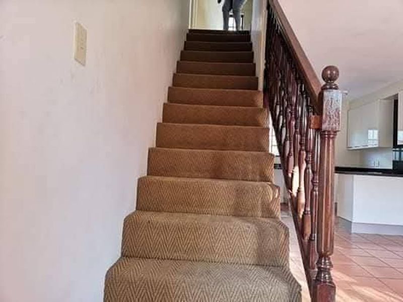 A staircase featuring a wooden balustrade and carpeted steps, leading to the upper level of the townhouse.