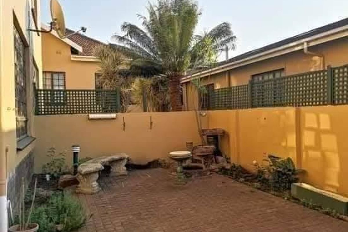 A private rear courtyard featuring paved flooring, boundary walls with trellis fencing, and established garden elements, offering a quiet outdoor space.