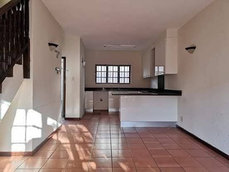 Open-plan kitchen and living area featuring tiled flooring, built-in cabinetry, a kitchen island, and a staircase with a wooden balustrade.