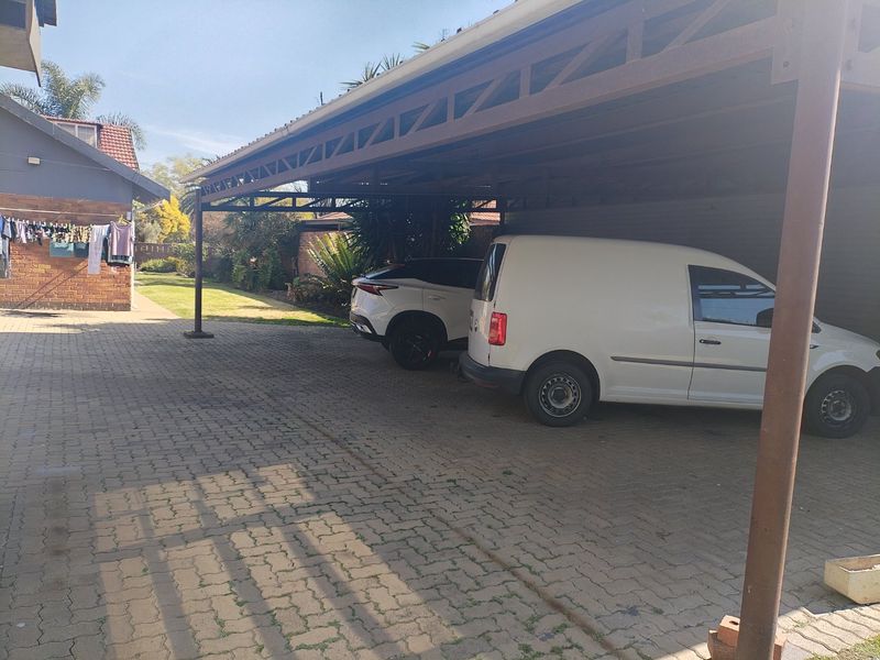 A covered carport area with paved driveway and metal structural framing, providing sheltered parking space.