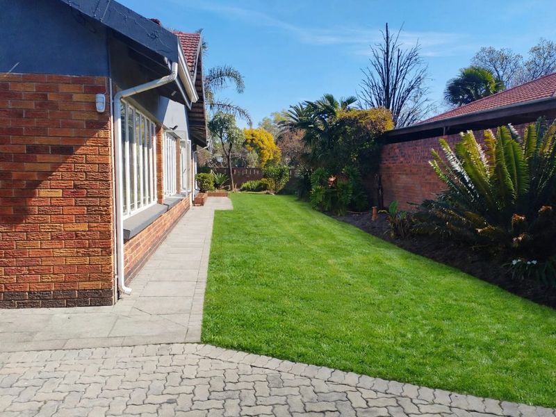 A well-maintained rear garden featuring a neat lawn, paved walkway, and established boundary walls alongside the brick exterior of the house.