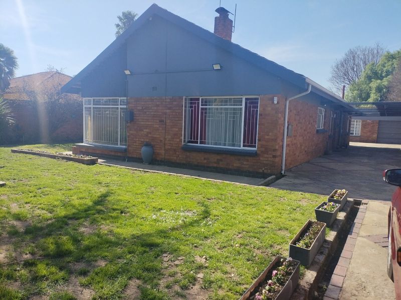 Front view of a single-story brick house featuring a tiled roof, security bars on windows, a driveway, and a carport.