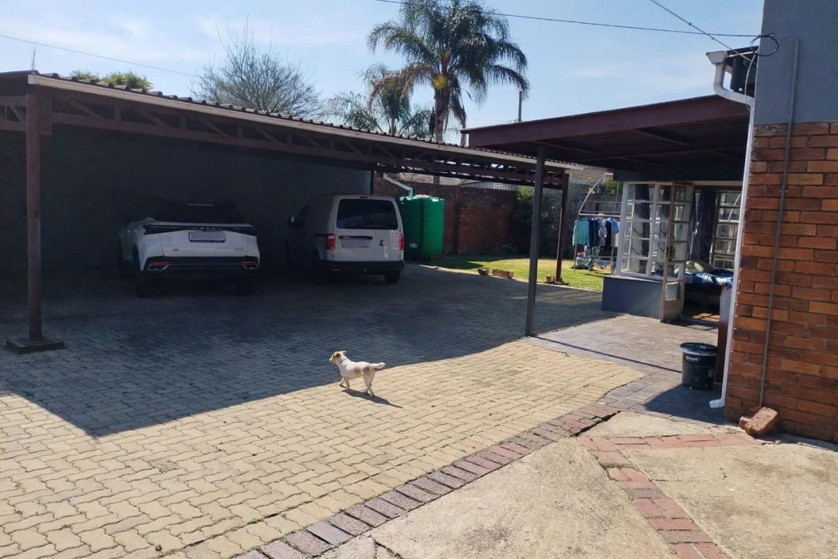 Rear exterior area featuring a large carport, paved driveway, and a covered patio space with brick walling.
