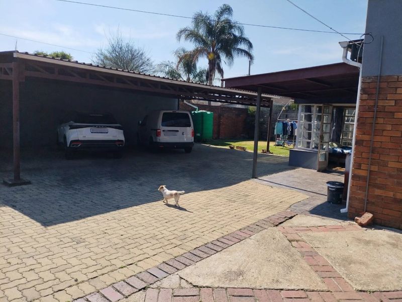 Rear exterior area featuring a large carport, paved driveway, and a covered patio space with brick walling.
