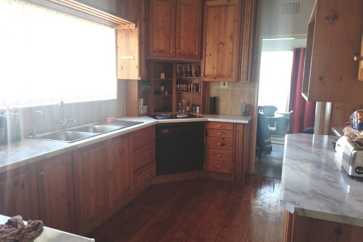 A functional kitchen featuring traditional wooden cabinetry, laminate countertops, a double bowl sink, and integrated oven with hob, set against hardwood flooring.