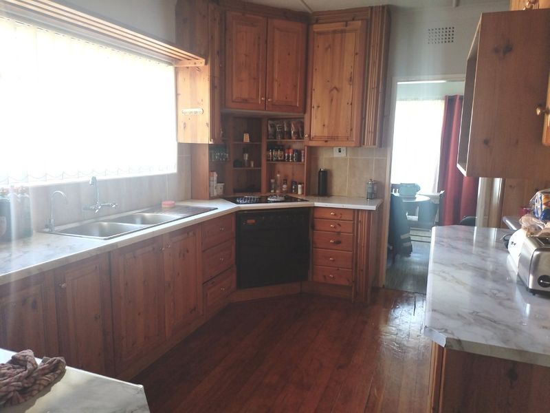 A functional kitchen featuring traditional wooden cabinetry, laminate countertops, a double bowl sink, and integrated oven with hob, set against hardwood flooring.