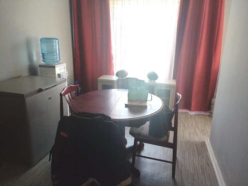 A dining area featuring laminate flooring and a large window with curtains, providing natural light to the space.