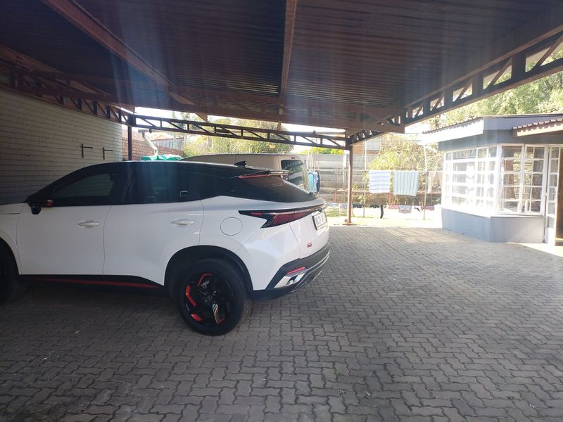A covered carport area with paved flooring, providing sheltered parking space adjacent to the main building structure.