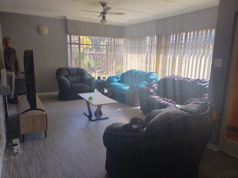 Spacious living room featuring laminate flooring, a ceiling fan, and large windows with vertical blinds and security bars.