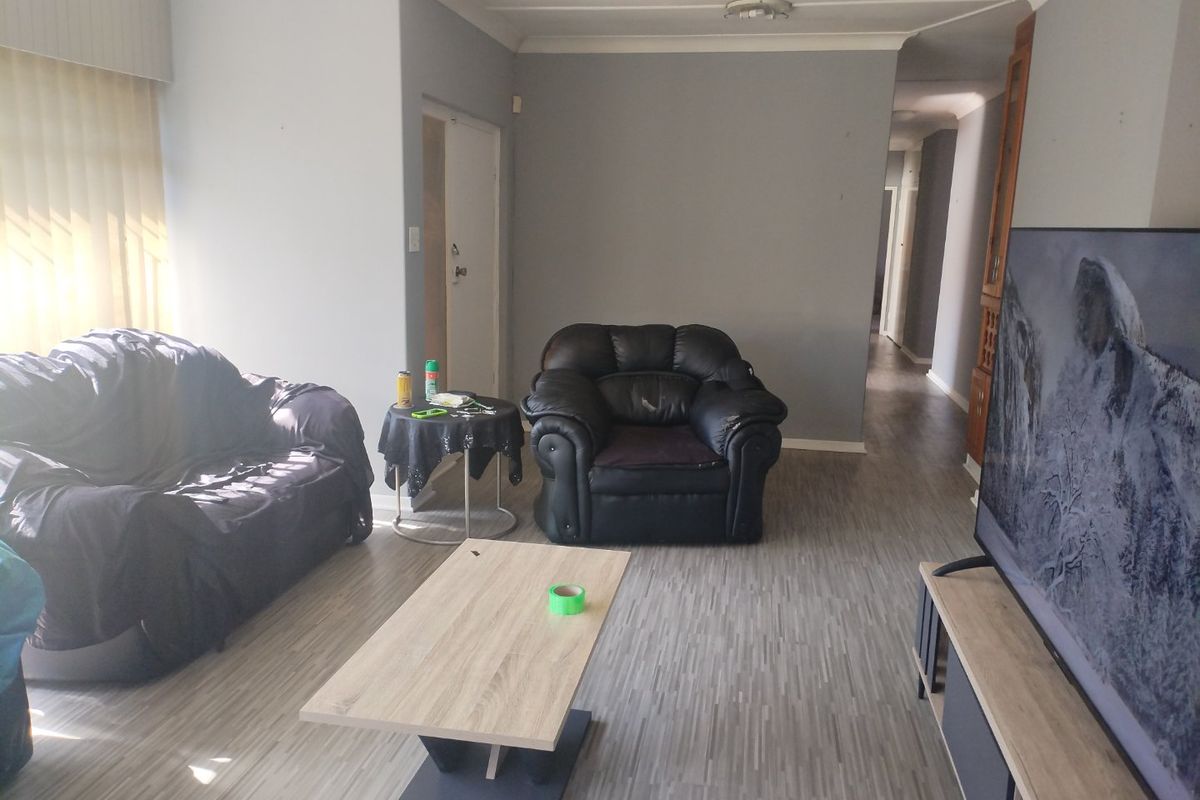 A living room featuring laminate flooring and neutral grey walls, providing a functional and open space with access to the hallway.