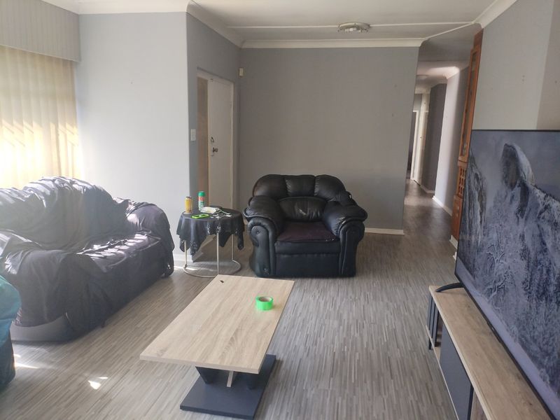 A living room featuring laminate flooring and neutral grey walls, providing a functional and open space with access to the hallway.