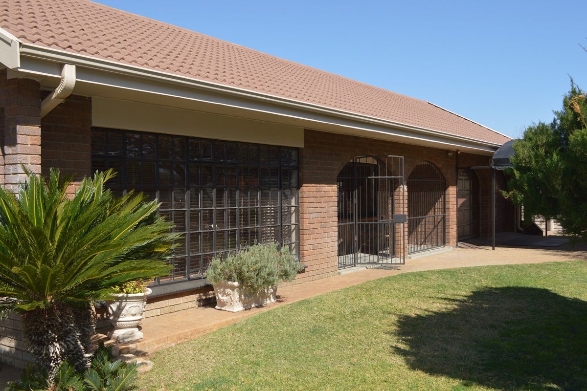 Rear view of a brick house featuring a tiled roof, steel-framed windows with security bars, and a paved walkway leading along the garden.